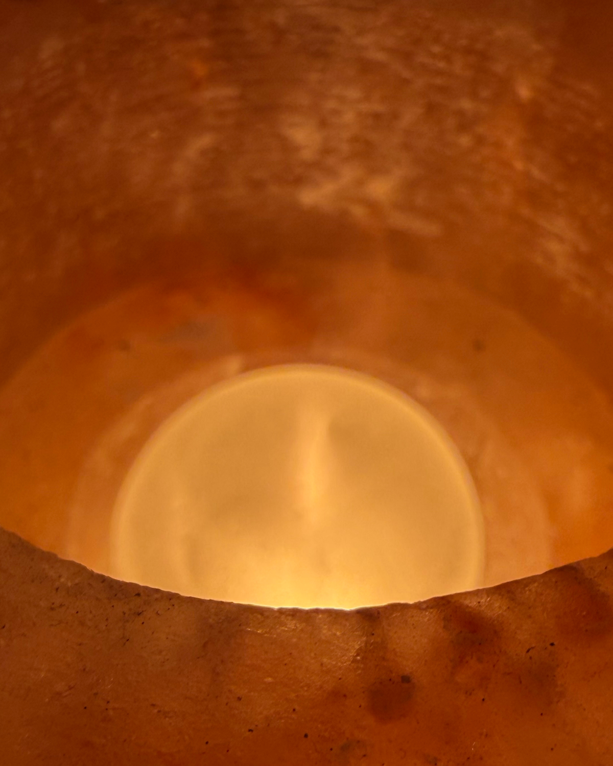 A close-up view from inside a warm, textured orange-brown container or candle holder, looking down toward a glowing round light source.