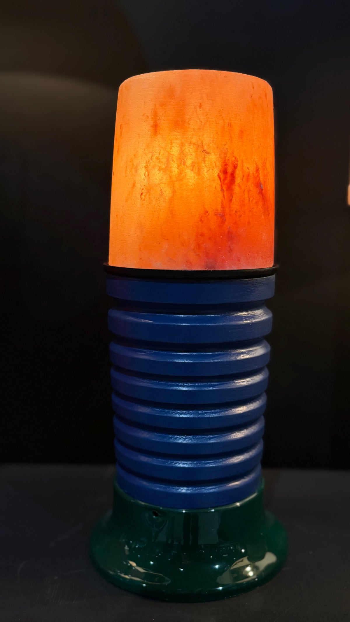 A decorative lamp with a glowing orange salt-look top, a ribbed blue middle section, and a dark green base, photographed against a dark background.